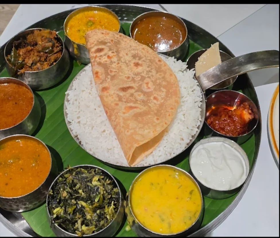 “South Indian vegetarian thali served on a banana leaf with steamed rice, papad, sambar, rasam, dal, vegetable curries, chutneys, pickle, yogurt, and traditional sweets.”